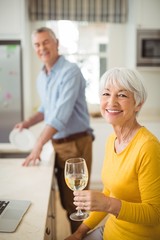 Happy senior woman holding glass of wine in kitchen 