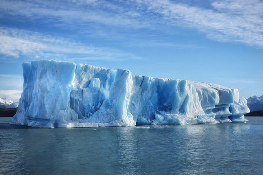 Single big blue iceberg in blue water in the center of the picture and blue sky with clouds on the background. Patagonia, Argentina