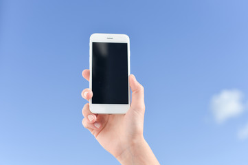 Holding mobile cell phone over blue sky white clouds background.