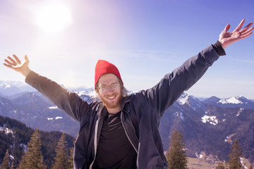 young bearded man surrounded by mountains stretching his arms