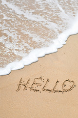 Hello sign word drawn on the outside sand beach with the soft foam wave