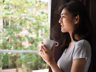 Young beautiful women holding a cup of coffee looing outside the window