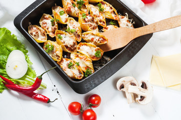 Italian pasta Conchiglioni Rigati stuffed with cheese and meat on white wood table