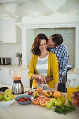 Happy couple embracing while preparing smoothie in kitchen
