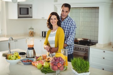 Happy couple embracing while preparing smoothie in kitchen