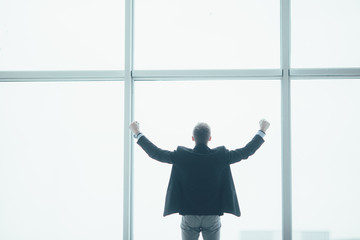 Stylish business man in rised hands victory in the background of a large window