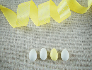 Cotton fabric background with yellow ribbon and candy in the form of eggs. Empty copy space for editor's content