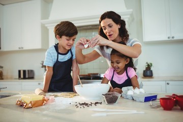 Mother and kids breaking egg in the bowl while preparing cookie