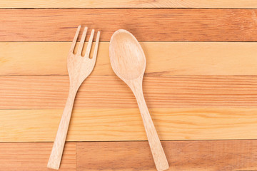 Top view of wooden fork and spoon on light wooden background.