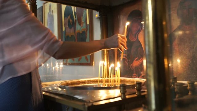 The woman puts a candle near the icon in monastery