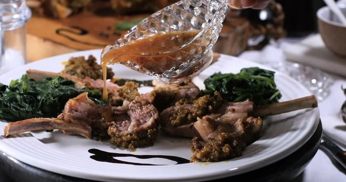 Pouring honey vinagrette over a rack of lamb in crusted mint sauce with spinach