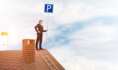 Young businessman with parking sign standing on brick roof. Mixed media