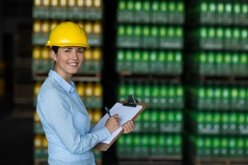 Female factory worker maintaining record on clipboard in factory