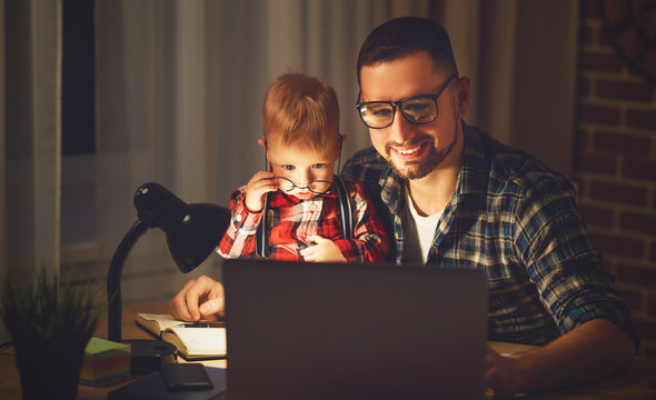 father and son baby work at home at computer in dark