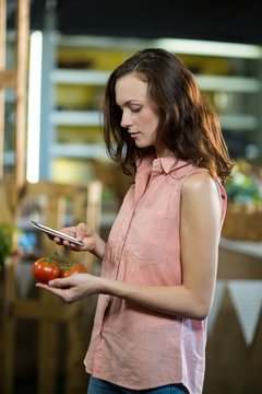 Woman using smartphone while holding tomatoes