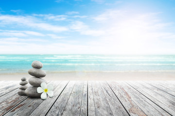 Stack of pebble stones and Plumeria at the beach on a wooden surface. Concept Zen, Spa, Summer, Beach, Sea, Relax. - obrazy, fototapety, plakaty