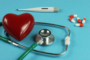 Stethoscope, thermometer and heart on blue background.
