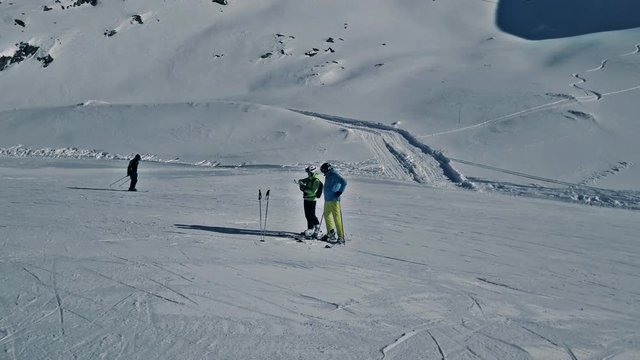 Father and daugther are standing on the hill and exploring the map. Scenic winter aerial flight of drone over the mountains and ski resort. Beautiful panorama, sunny day. Obergurgl, Austria. 4K. 