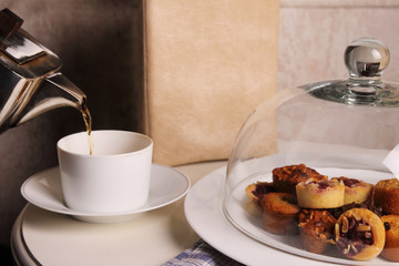 Tea is poured from the kettle into the cup. on the table, a plate of cake and menu. copy space.