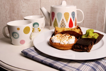Teapot and a cup on the table and a white plate with a variety of cakes. Homemade pastries.