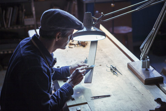 Carpenter using utility knife with wood at table in workshop