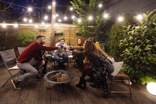 Happy friends toasting drinks in party at night