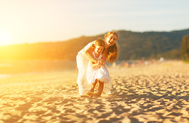 happy family at beach. mother and child daughter run, laugh and play at sunset