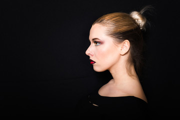Blonde with hair gathered in a bun and professional make-up with dark red lips on a dark background