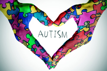text autism and hands forming a heart with puzzle pieces - obrazy, fototapety, plakaty