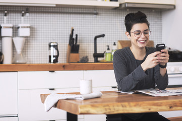 Smiling woman using smartphone at dining table in home