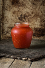 Tomato sauce in a transparent jar on a wooden surface