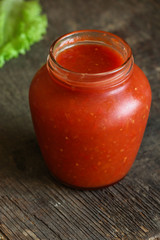 Tomato sauce in a transparent jar on a wooden surface
