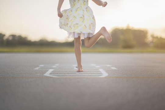 Low section of girl playing hopscotch on footpath against sky