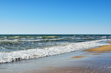 Sea waves wash the beach against a blue sky