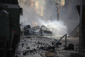 Car in flames extinguished by a police water cannon truck.
Street damage caused during a student...