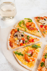 Slices of two kinds of dietary vegetarian pizza on a white stone table: with mushrooms and shrimps.With white wine in glass, copy space