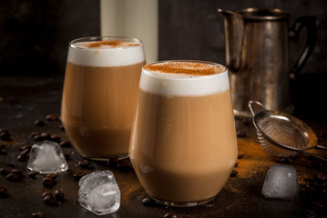 Morning. Breakfast. Classic summer cold coffee latte with whipped milk, ice and cinnamon. On  black background. Milk, coffee pot, strainer for strewing. Close view