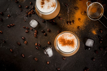 Morning. Breakfast. Classic summer cold coffee latte with whipped milk, ice and cinnamon. On  black background. Milk, coffee pot, strainer for strewing. Copy space top view