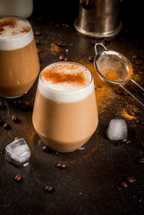 Morning. Breakfast. Classic summer cold coffee latte with whipped milk, ice and cinnamon. On  black background. Milk, coffee pot, strainer for strewing. Copy space vertical