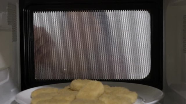 Woman heating fast food chicken nuggets in the microwave at home