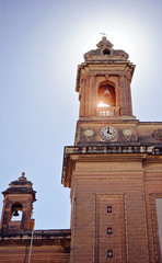 Bottom view of the two towers of the church with a bell and a clock on the blue sky background, Senglea Basilica, Malta