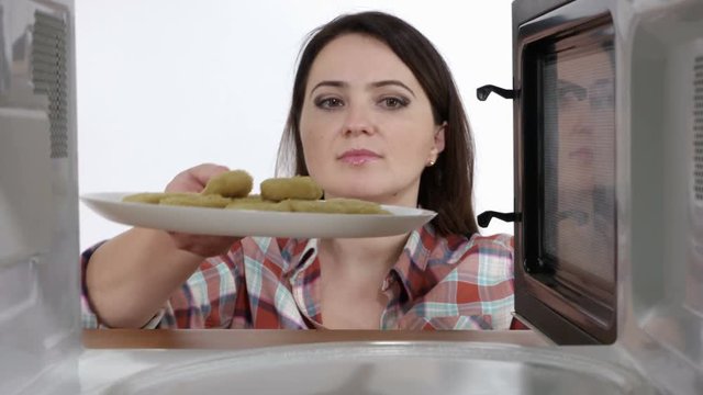 Woman heating fast food in the microwave at home. Rotating chicken nuggets inside microwave oven