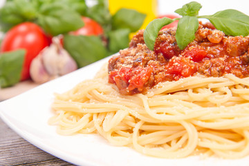 Spaghetti bolognese,some tomatoes, olive oil, basil, garlic, and raw pasta in the background