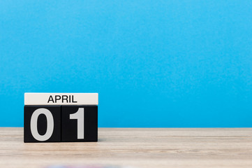 April 1st. Day 1 of month, calendar on wooden table and blue background. Spring time, empty space for text
