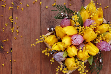 Flower arrangement of tulips, mimosas and willows on a wooden table