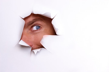 A curious eye looks into the torn hole on a white sheet
