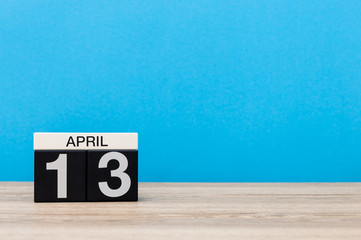April 13th. Day 13 of month, calendar on wooden table and blue background. Spring time, empty space for text
