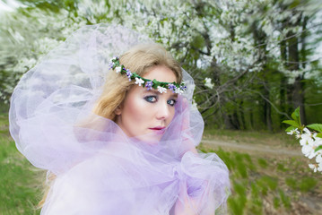 beautiful young blonde girl in blooming trees in spring