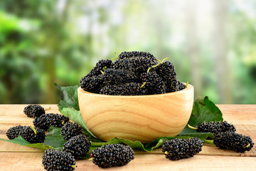 Mulberries on wooden table and blurred nature background.