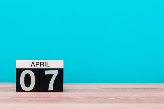 April 7th. Day 7 of month, calendar on wooden table and turquoise background. Spring time, empty space for text